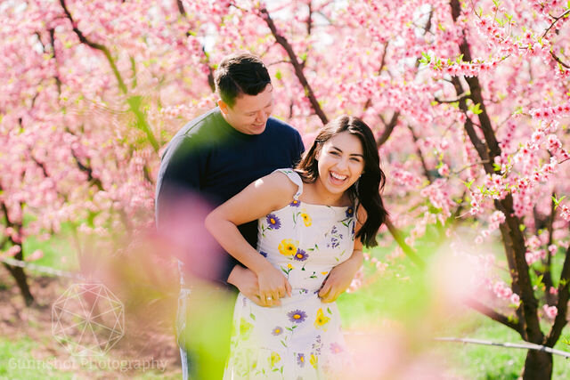 Man tickles woman from behind in the midst of flower blossoms.