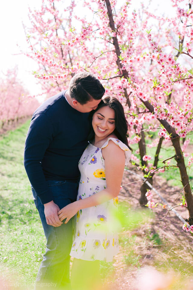 Man snuggling woman in floral dress in pink orchard
