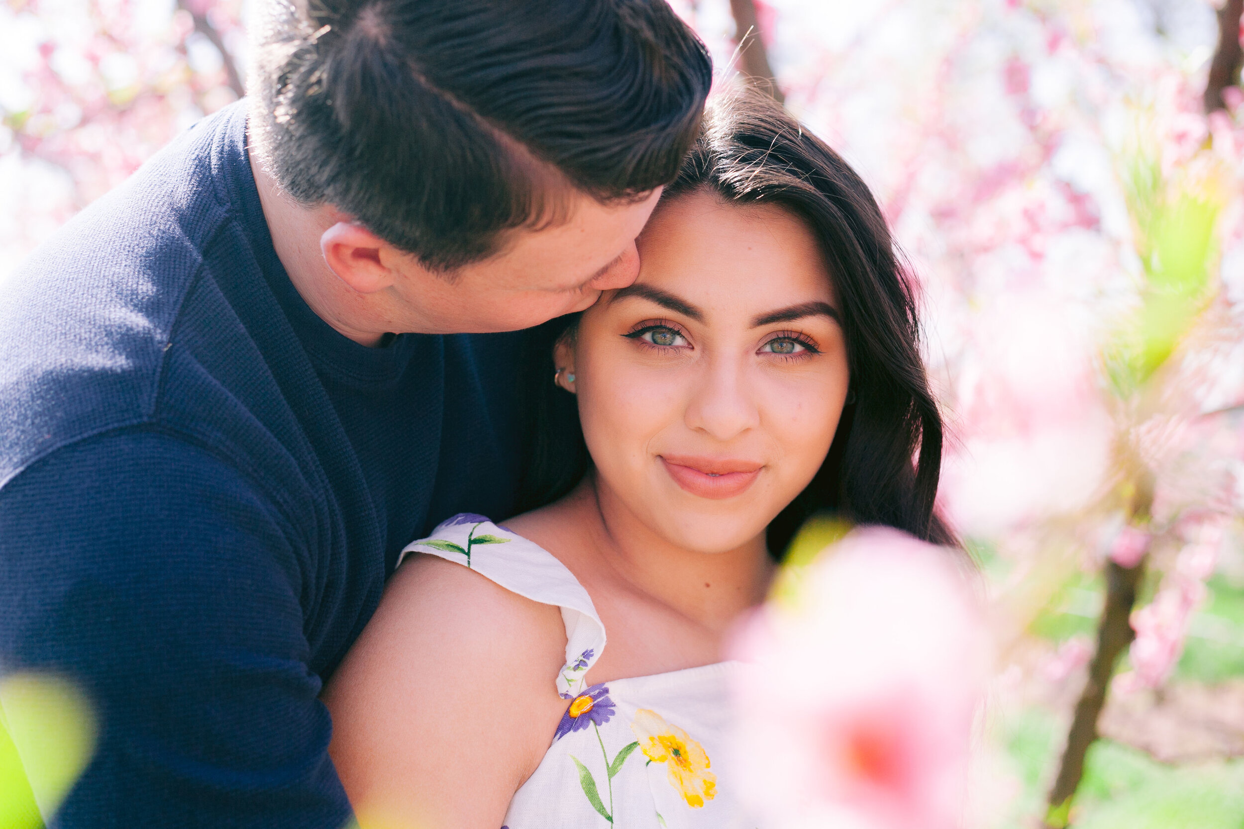 Man kissing woman on the side of the head in flower field.