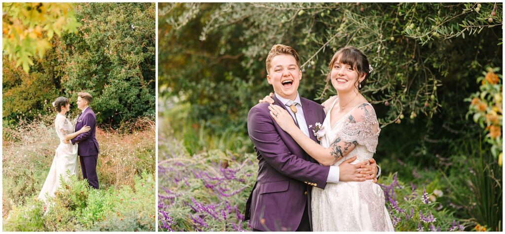 Two brides laughing at the camera, one bride in a purple suit with short hair, the other bride in a white dress. 