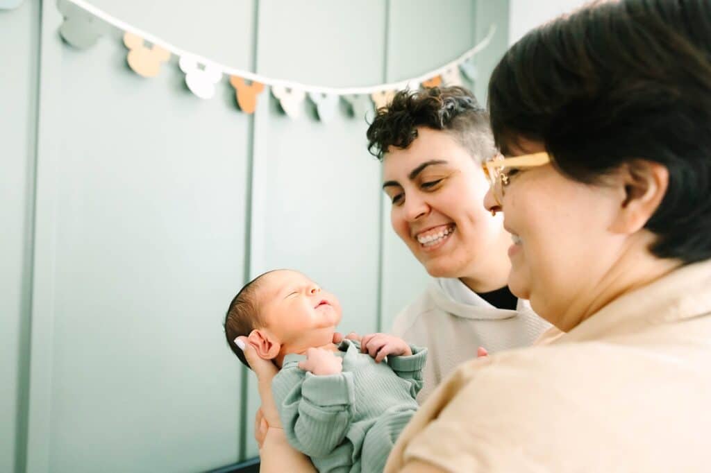 One parent holding a newborn while the other smiles nearby during a Fresno family photo session, illustrating shared care and joy from Fresno family photo tips.