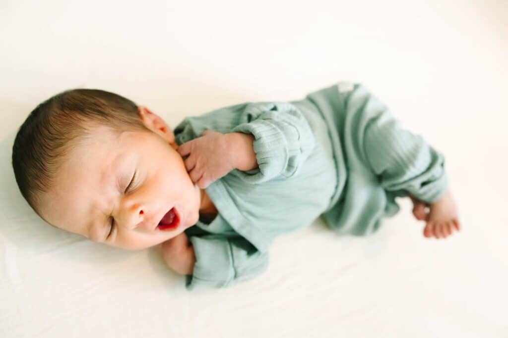 A newborn baby sleeping peacefully in a soft green outfit on a white bed during a Fresno family photo session, highlighting calm newborn moments from Fresno family photo tips.