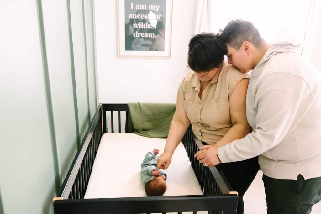 Two parents leaning over a crib, smiling and gently touching their newborn during a Fresno family photo session, showing intimate in-home moments from Fresno family photo tips.
