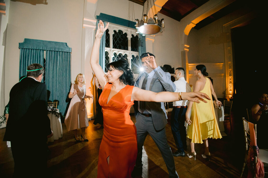 Guest in a red dress dances with arms raised while others celebrate on the dance floor at a Berkley City Club wedding reception, captured by Michelle Gunn Photo at a joyful lesbian wedding.