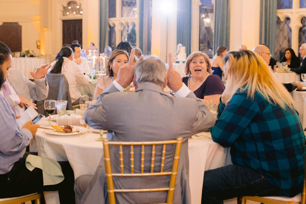 Candid moment of guests laughing and gesturing at a reception table inside the Berkley City Club wedding venue, captured by Michelle Gunn Photo during a lively lesbian wedding reception.