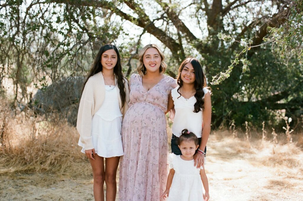 A parent standing with two older children and a toddler in a sunlit field during a Fresno family photo session on 35mm film, capturing a calm family portrait from Fresno Family Photo Tips.