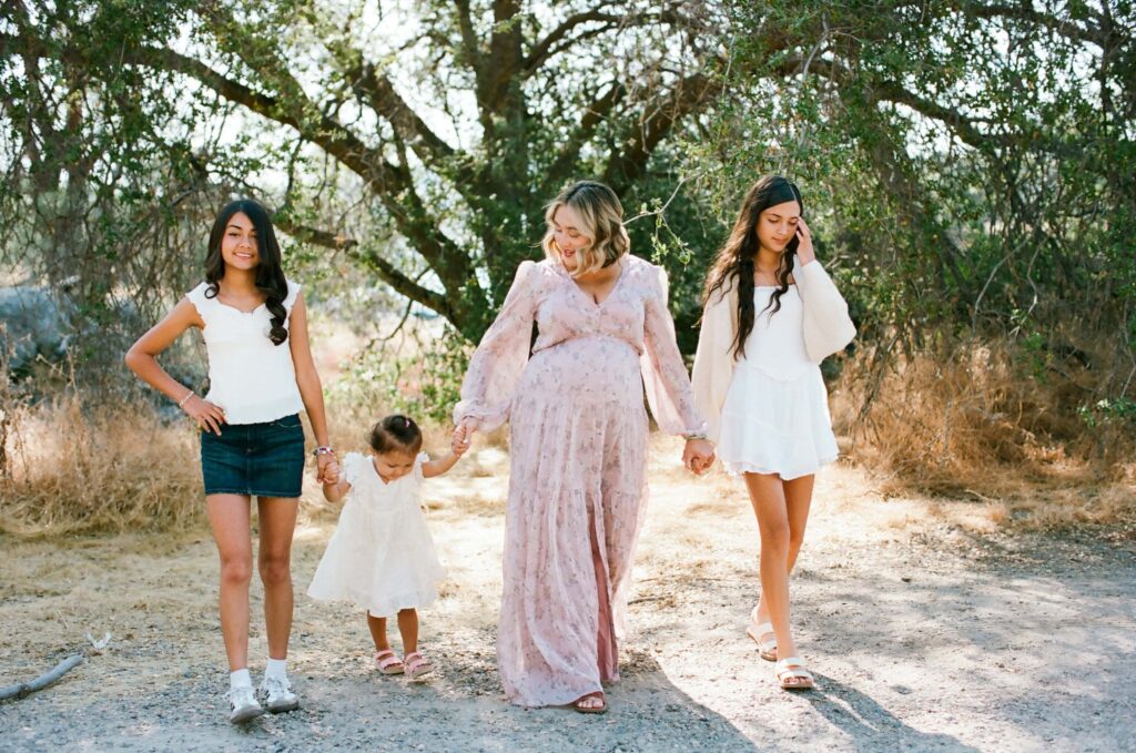 A parent walking hand in hand with three children along a sunlit trail beneath oak trees during a Fresno family photo session on 35mm film, showing natural movement from Fresno Family Photo Tips.