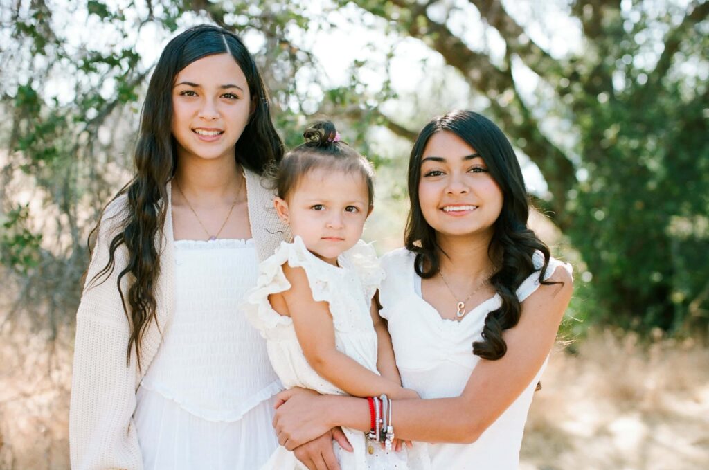 Two older siblings holding a toddler between them and smiling at the camera during a Fresno family photo session on 35mm film, showing sibling closeness from Fresno Family Photo Tips.