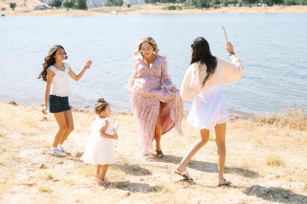 Four family members dancing and playing near the lake during a Fresno family photo session, capturing spontaneous joy from Fresno family photo tips.
