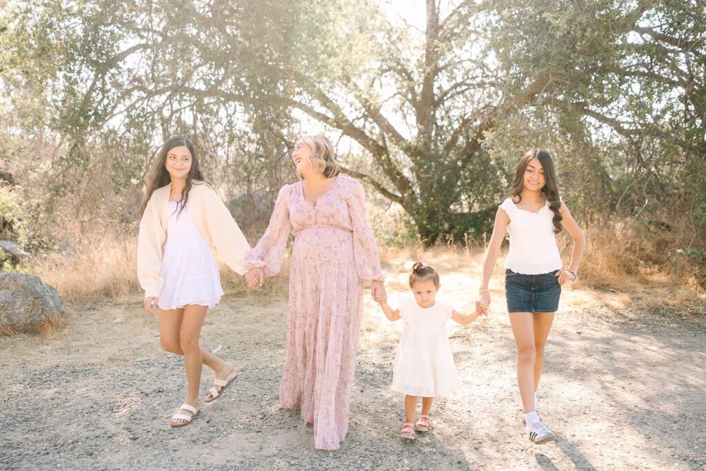 A parent and three children walking together holding hands on a sunlit trail during a Fresno family photo session, demonstrating candid family movement from Fresno family photo tips.