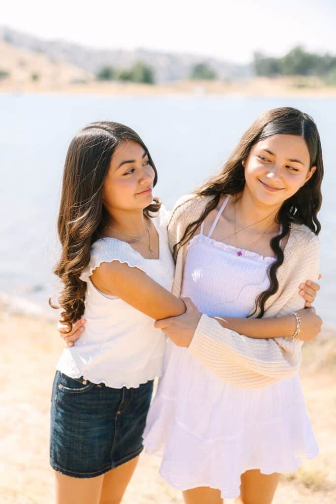 Two siblings hugging and smiling together by the lake during a Fresno family photo session, showing sibling connection from Fresno family photo tips.