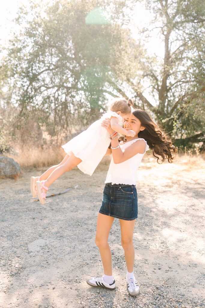 An older child lifting a younger child into the air while playing outdoors near a lake during a Fresno family photo session, capturing joyful motion from Fresno family photo tips.