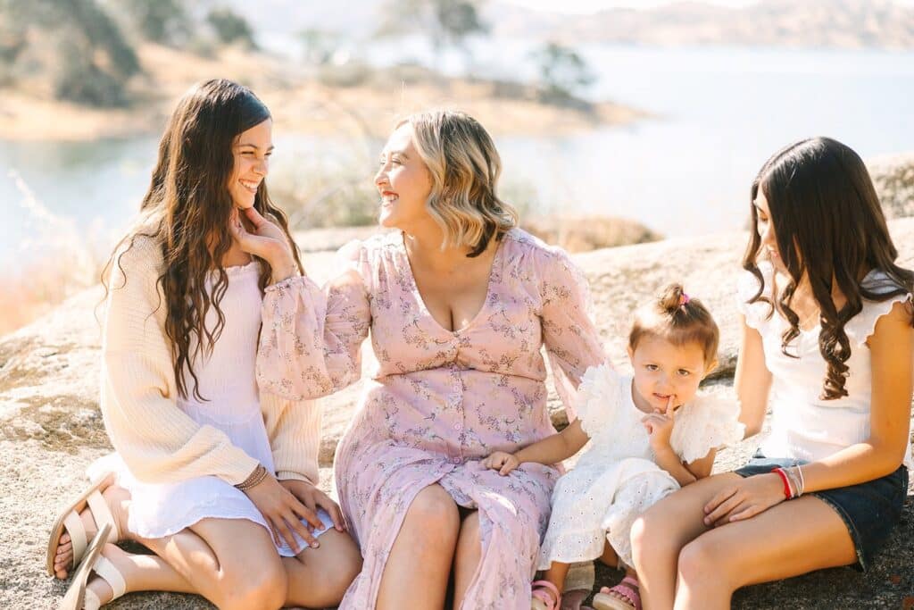 A parent sitting on a rock with three children beside a lake, laughing together during a Fresno family photo session, highlighting relaxed interaction from Fresno family photo tips.