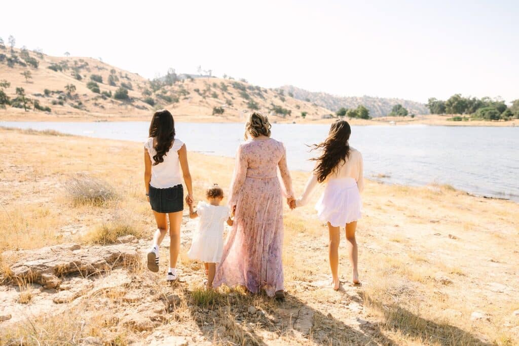 A parent and three children walking hand in hand toward a lake during a Fresno family photo session, showing natural movement and connection from Fresno family photo tips.