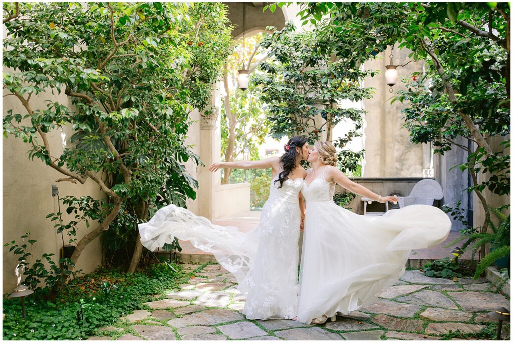 Brides twirling in a garden courtyard at a Berkley City Club wedding, photographed by Michelle Gunn Photo during a vibrant lesbian wedding celebration.