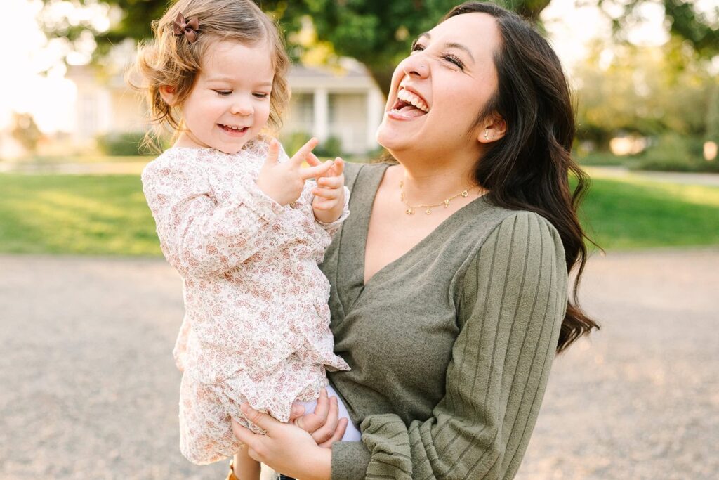 A parent laughing while holding their toddler daughter during a relaxed outdoor Fresno family photo session, showing candid connection featured in Fresno family photo tips.