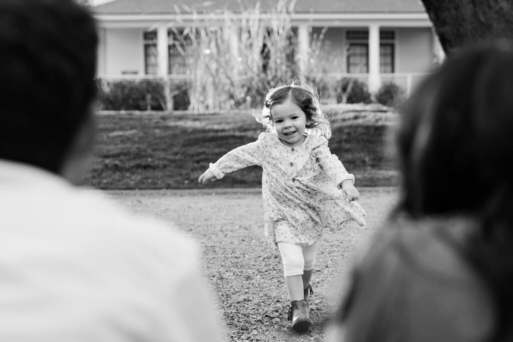 Black and white photo of a toddler running toward her parents with arms open during a Fresno family photography session, capturing movement and emotion in Fresno family photo tips.