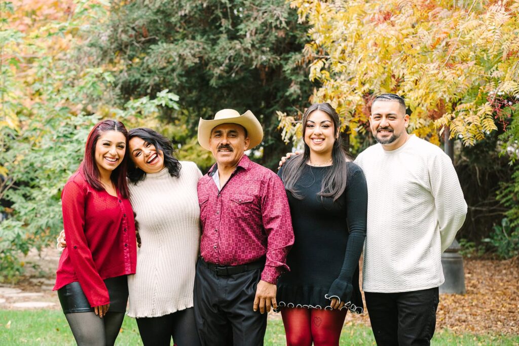 Five family members standing close together in a park with autumn leaves during a Fresno family photo session, showing relaxed group posing from Fresno family photo tips.
