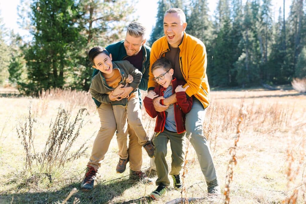 Two parents playfully holding their laughing children during a Fresno family session in a sunlit meadow, capturing energy and joy from Fresno family photo tips.