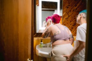 LGBTQ+ couple laughing and embracing with vibrant hair colors during Fresno wedding prep