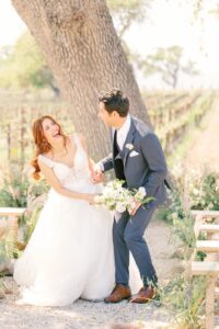 Bride and groom laughing together during their outdoor Fresno wedding ceremony, surrounded by greenery and vineyard rows