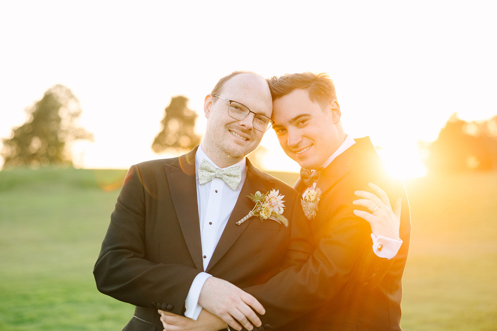 Groom and groom embracing at sunset during their Eagle Vines Golf Club wedding in Napa Valley, wearing tuxedos with floral boutonnieres