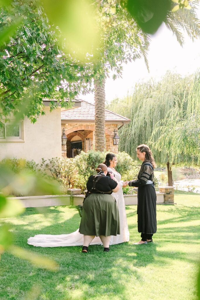 Outdoor wedding ceremony on a green lawn with officiant and couple exchanging vows beneath leafy trees, photographed by michelle gunn photo.
