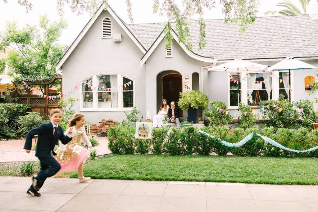 Children running on the sidewalk in front of a decorated home during a relaxed Porchfest Fresno wedding in the Tower District.