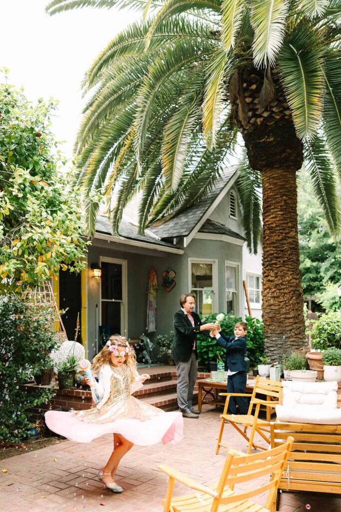Girl spinning in a gold dress blowing bubbles in a front yard during a Porchfest Fresno wedding celebration in the Tower District.